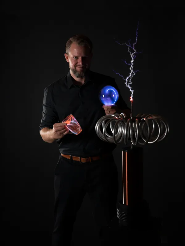 Thomas Sandner mit Plasmakugel und leuchtendem Glas neben der Teslaspule
